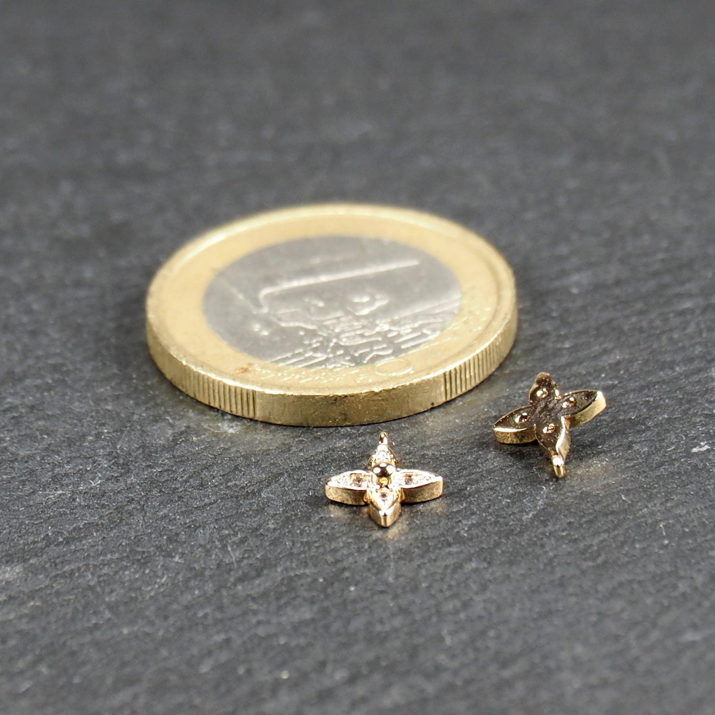 Vierblättriger goldfarbener Anhänger mit vier eingelassenen klaren Steinchen und zentraler Kugel, Öse sichtbar; daneben 1‑Euro‑Münze.