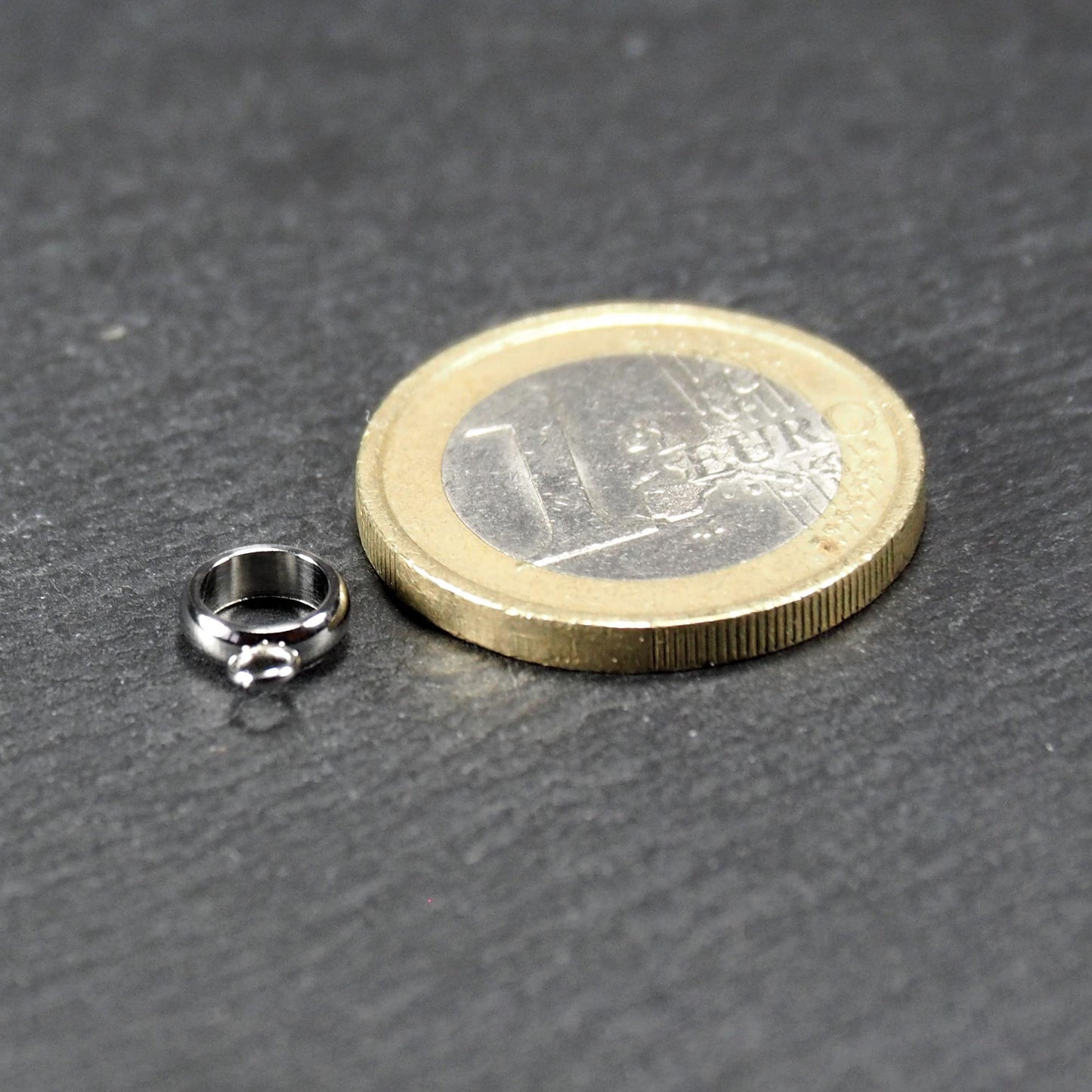 Runde, silberfarbene Anhängeröse mit glänzender Oberfläche und kleinem angehängtem Ösenring, neben einer 1-Euro-Münze.