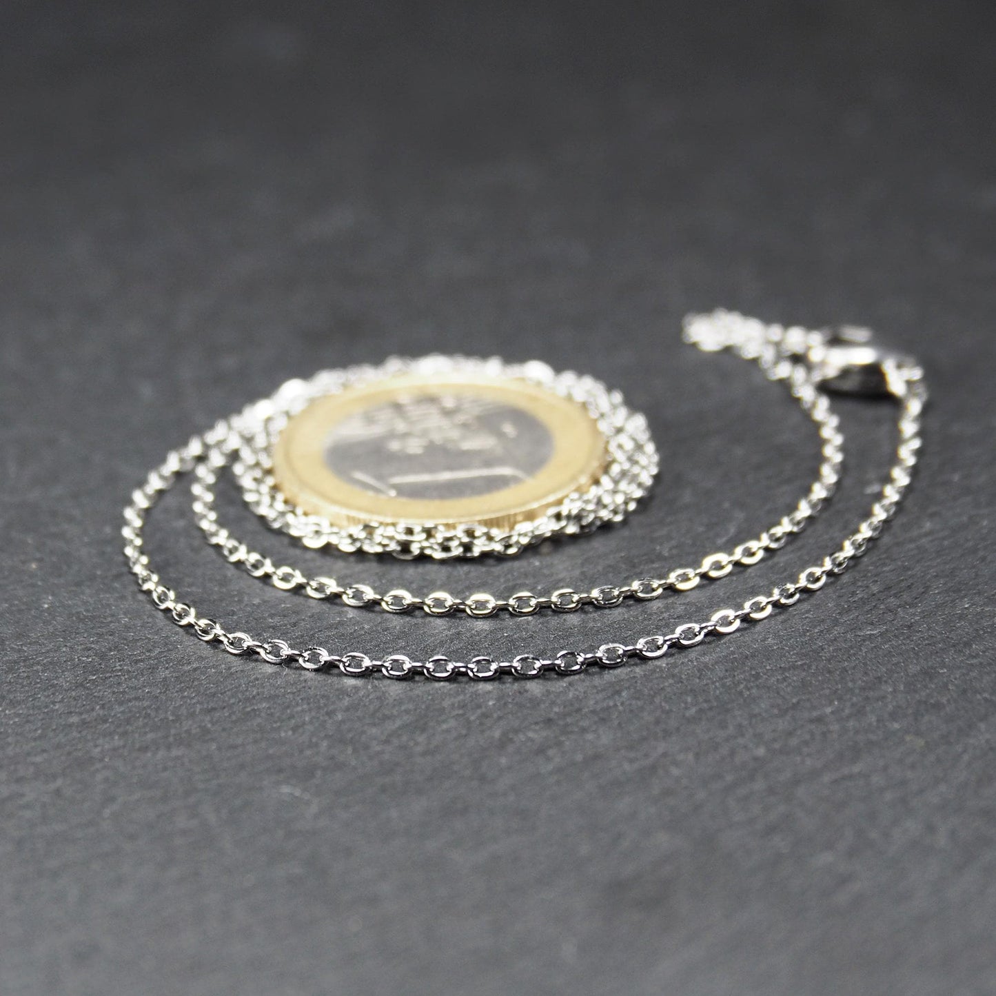 Eine Ankerkette hat filigrane offene Ankerglieder, polierte silberne Oberfläche und einen sichtbaren Karabinerverschluss.