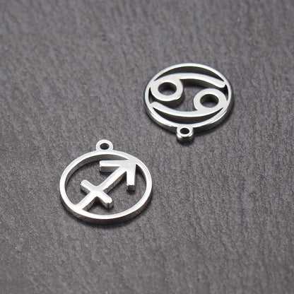 Zwei runde silberne Metallanhänger mit durchbrochenen Sternzeichensymbolen (Krebs, Schütze) und sichtbarer integrierter Öse auf dunklem Hintergrund.