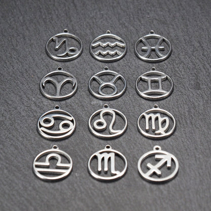 Zwölf runde silberne Anhänger mit durchbrochenen Sternzeichenmotiven, glänzende Oberfläche, integrierte Öse, auf dunklem strukturiertem Untergrund.