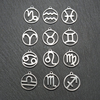 Zwölf runde silberne Anhänger mit durchbrochenen Sternzeichenmotiven, glänzende Oberfläche, integrierte Öse, auf dunklem strukturiertem Untergrund.