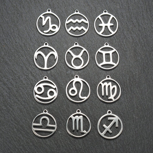 Zwölf runde silberne Anhänger mit durchbrochenen Sternzeichenmotiven, glänzende Oberfläche, integrierte Öse, auf dunklem strukturiertem Untergrund.