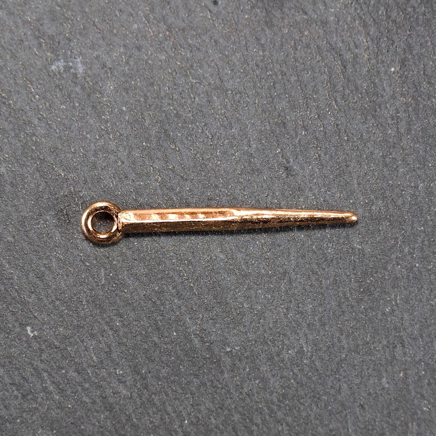 Konischer goldfarbener Anhänger mit glänzender Oberfläche, viereckigem, spitz zulaufendem Schaft und sichtbarer Öse.