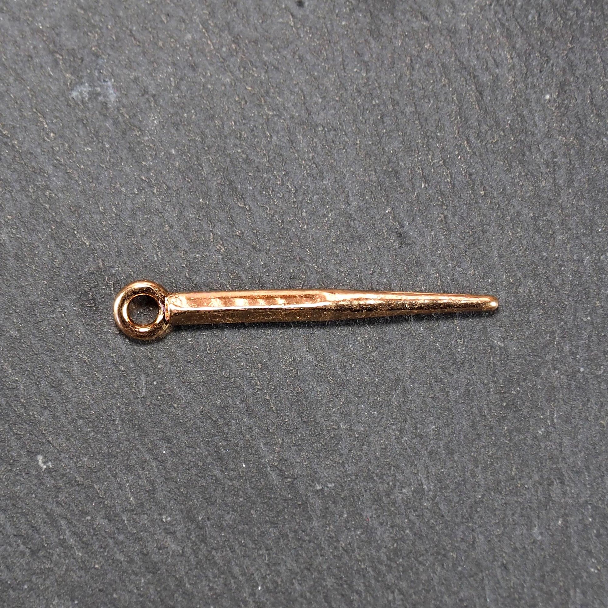 Konischer goldfarbener Anhänger mit glänzender Oberfläche, viereckigem, spitz zulaufendem Schaft und sichtbarer Öse.