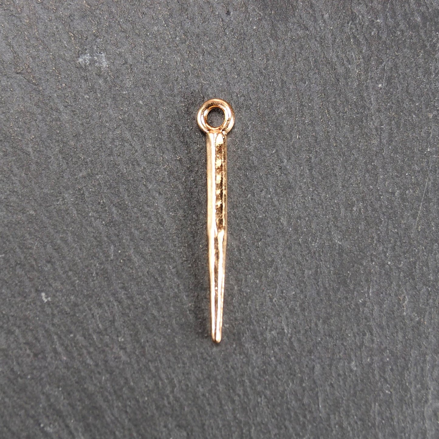 Konischer goldfarbener Anhänger mit glänzender Oberfläche, viereckigem, spitz zulaufendem Schaft und sichtbarer Öse.