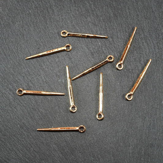 Mehrere Anhänger, goldfarben glänzend, konisch mit spitz zulaufender Form und sichtbarer Öse, flach facettierte Vierkantprofile.