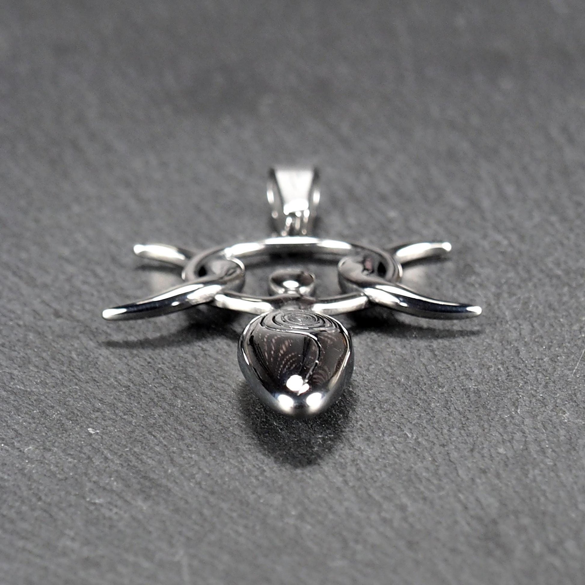 Anhänger aus poliertem silberfarbenem Edelstahl in figürlicher Form mit durchbrochenem Dreifachmond-Motiv, Spirale und Anhängerschlaufe.