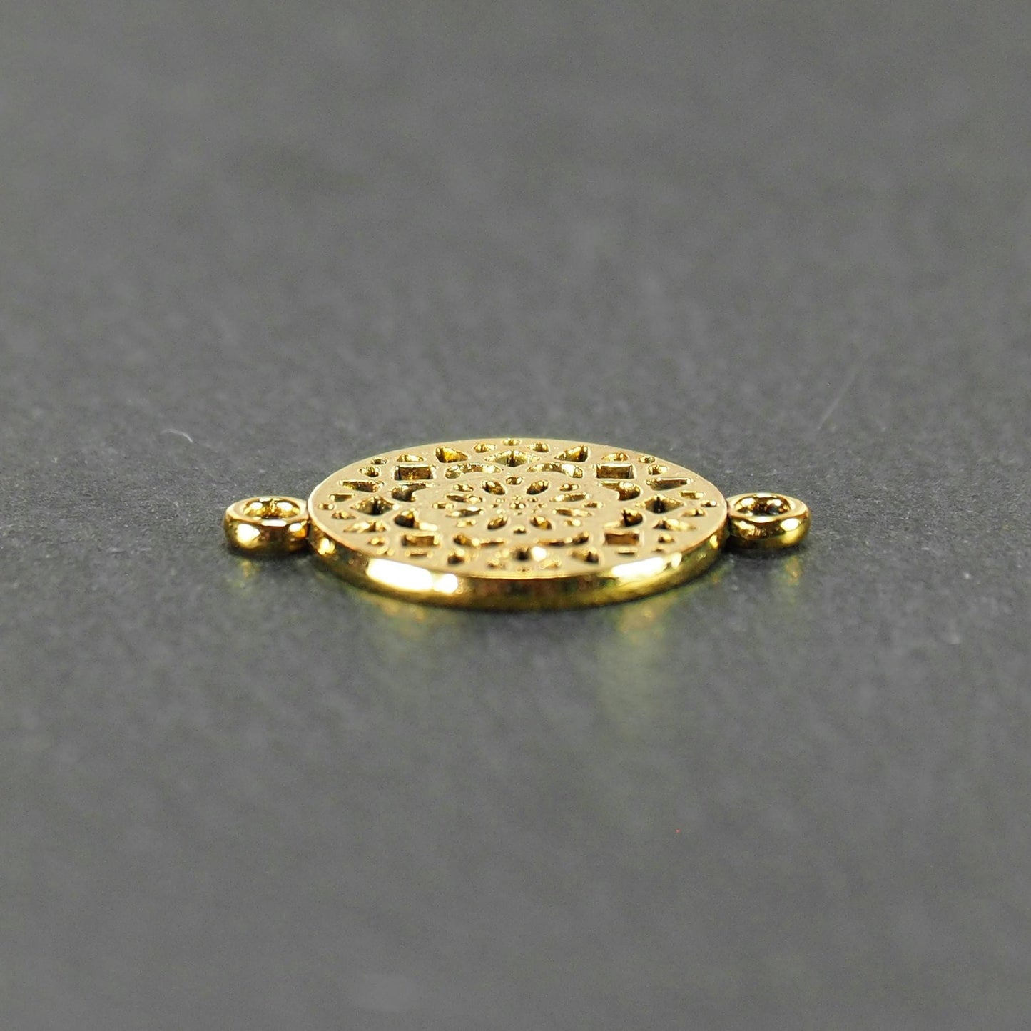 Runder goldfarbener Verbinder mit durchbrochenem, radial-symmetrischem Mandala-/Blütenmuster und zwei gegenüberliegenden Ösen.