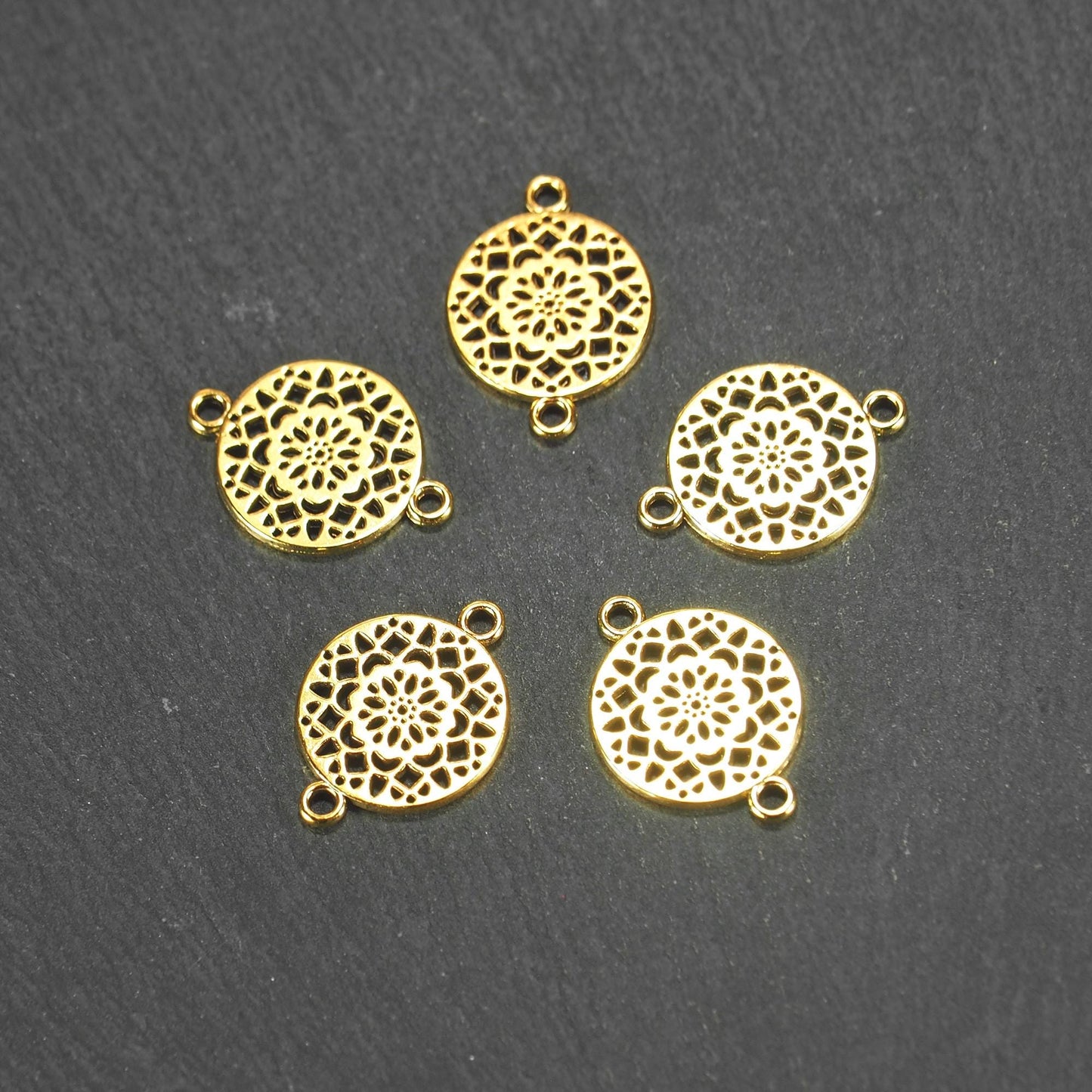 Fünf runde goldfarbene Verbinder mit durchbrochenem, radial-symmetrischem Mandala- bzw. Blütenmuster und je zwei Ösen.