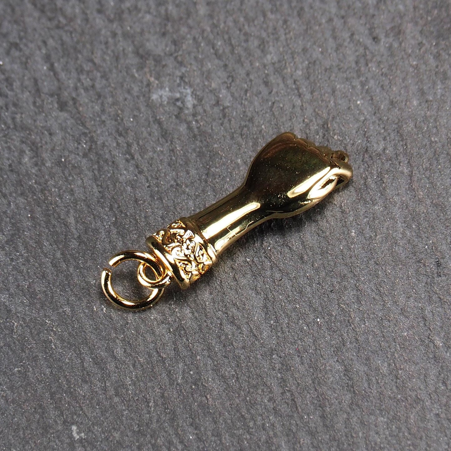 Goldfarbener Anhänger in Figa-Hand-Form mit glänzender Oberfläche, fein gravierter ornamentaler Manschette und kleiner Anhängeröse.