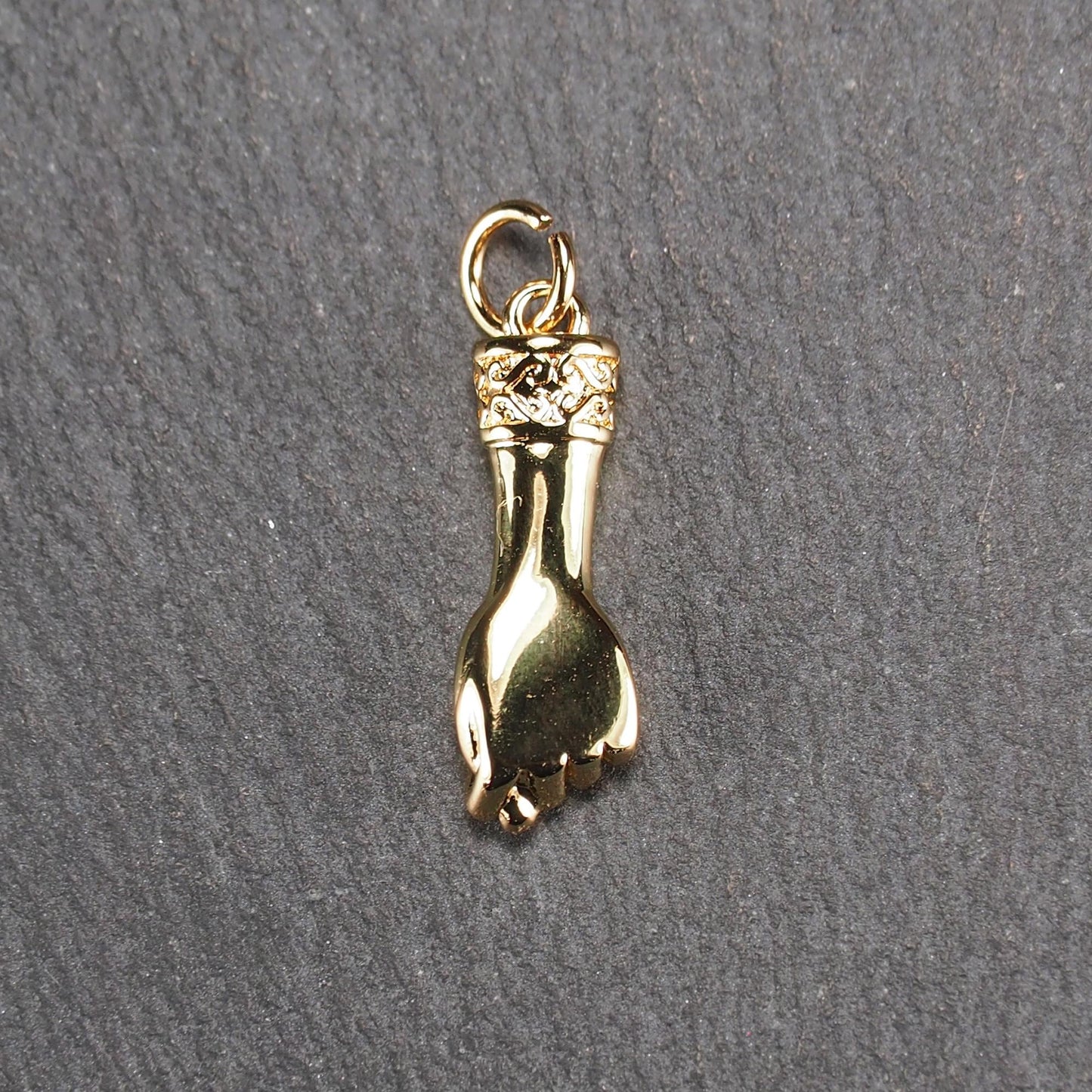 Goldfarbener Anhänger in Figa-Hand-Form mit glänzender Oberfläche, fein gravierter ornamentaler Manschette und kleiner Anhängeröse.