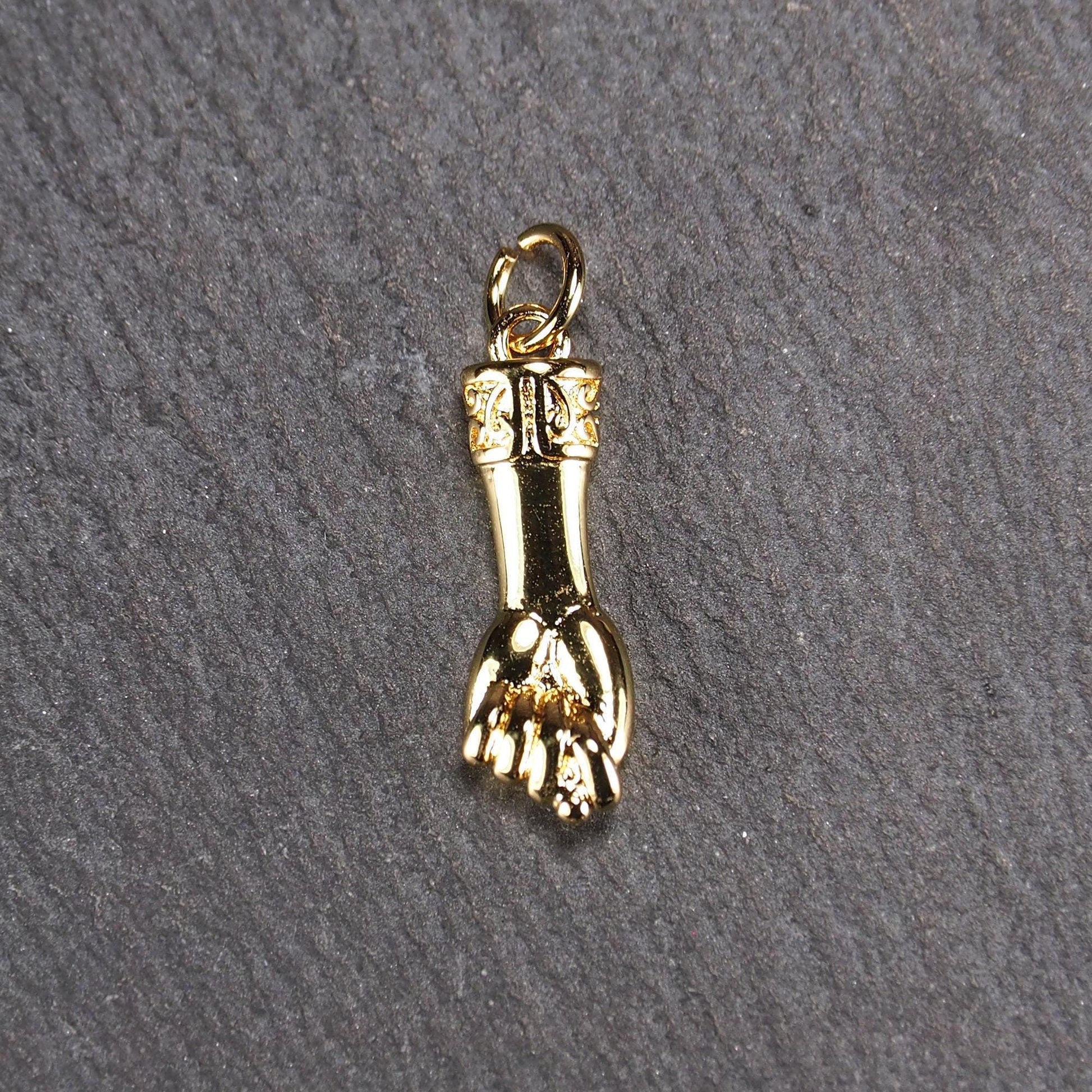Goldfarbener Anhänger in Figa-Hand-Form mit glänzender Oberfläche, fein gravierter ornamentaler Manschette und kleiner Anhängeröse.
