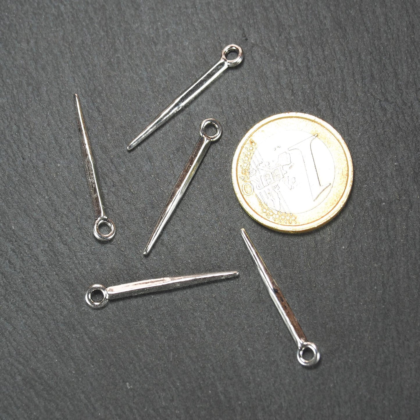 Konischer, silbern glänzender Anhänger mit spitz zulaufender, leicht vierkantiger Form und kleiner Öse, neben einer 1-Euro-Münze zur Größenangabe.
