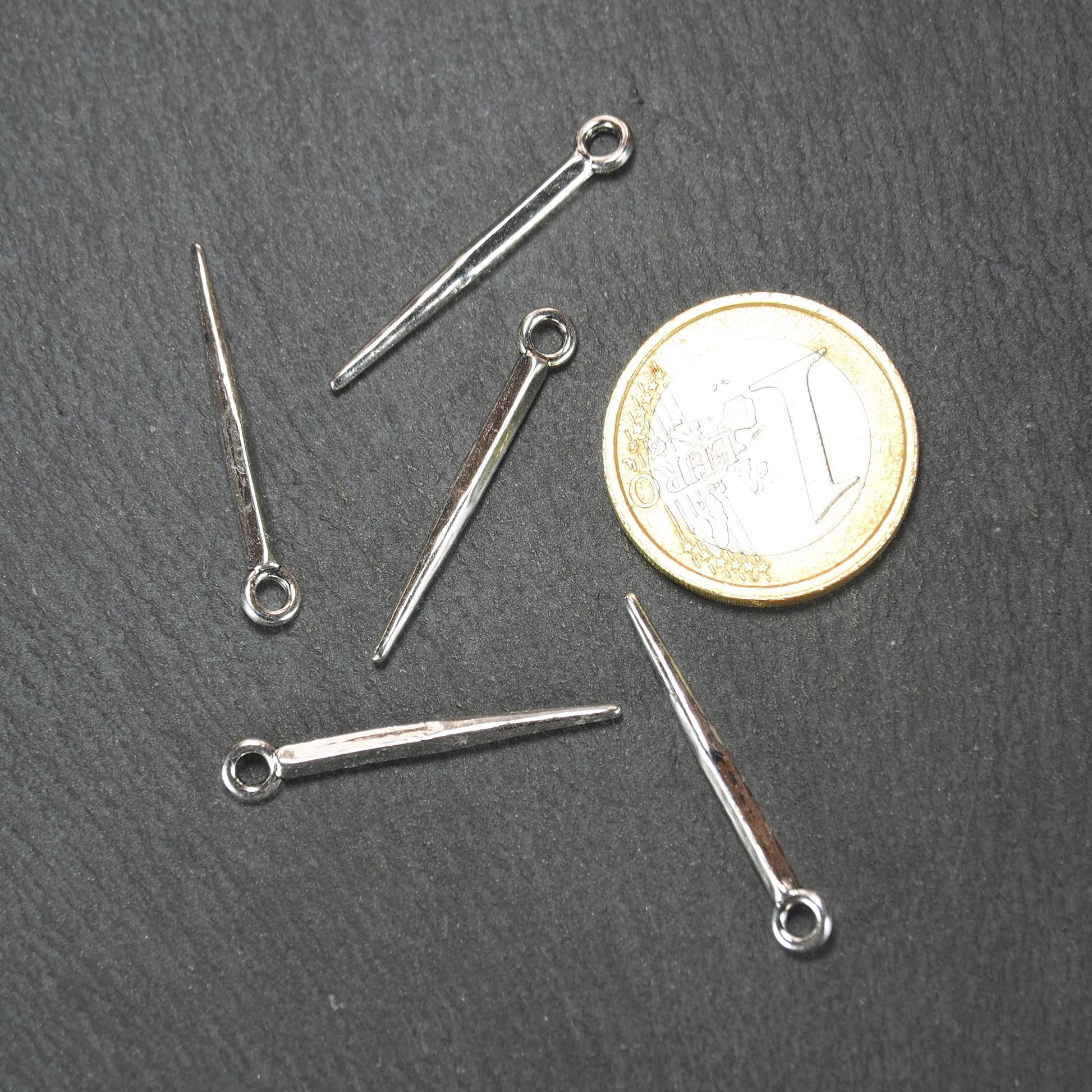 Konischer, silbern glänzender Anhänger mit spitz zulaufender, leicht vierkantiger Form und kleiner Öse, neben einer 1-Euro-Münze zur Größenangabe.