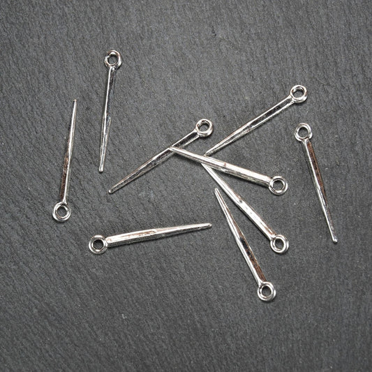 Mehrere silberfarbene, glänzende konische Anhänger mit spitz zulaufendem, viereckigem Schaft und kleiner Öse am breiten Ende auf dunklem Untergrund.