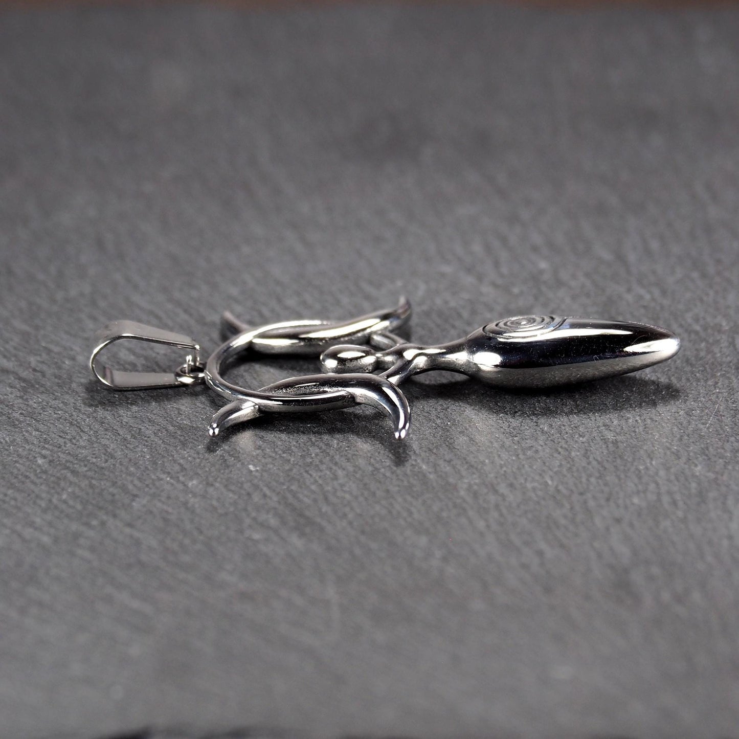 Anhänger aus poliertem silberfarbenem Edelstahl in figürlicher Form mit durchbrochenem Dreifachmond-Motiv, Spirale und Anhängerschlaufe.