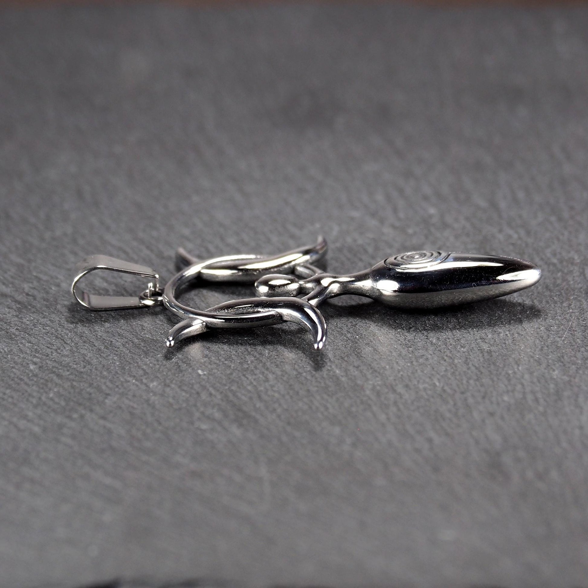 Anhänger aus poliertem silberfarbenem Edelstahl in figürlicher Form mit durchbrochenem Dreifachmond-Motiv, Spirale und Anhängerschlaufe.