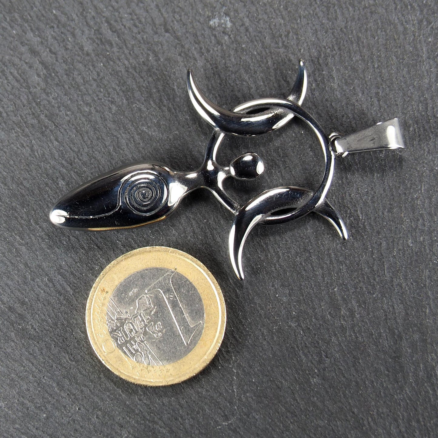 Figürlicher silberner, polierter Anhänger mit durchbrochenem Kreis, drei Mondsicheln, ovalem Kopf mit Spirale und Aufhängeöse; Ein-Euro-Münze als Größenvergleich.