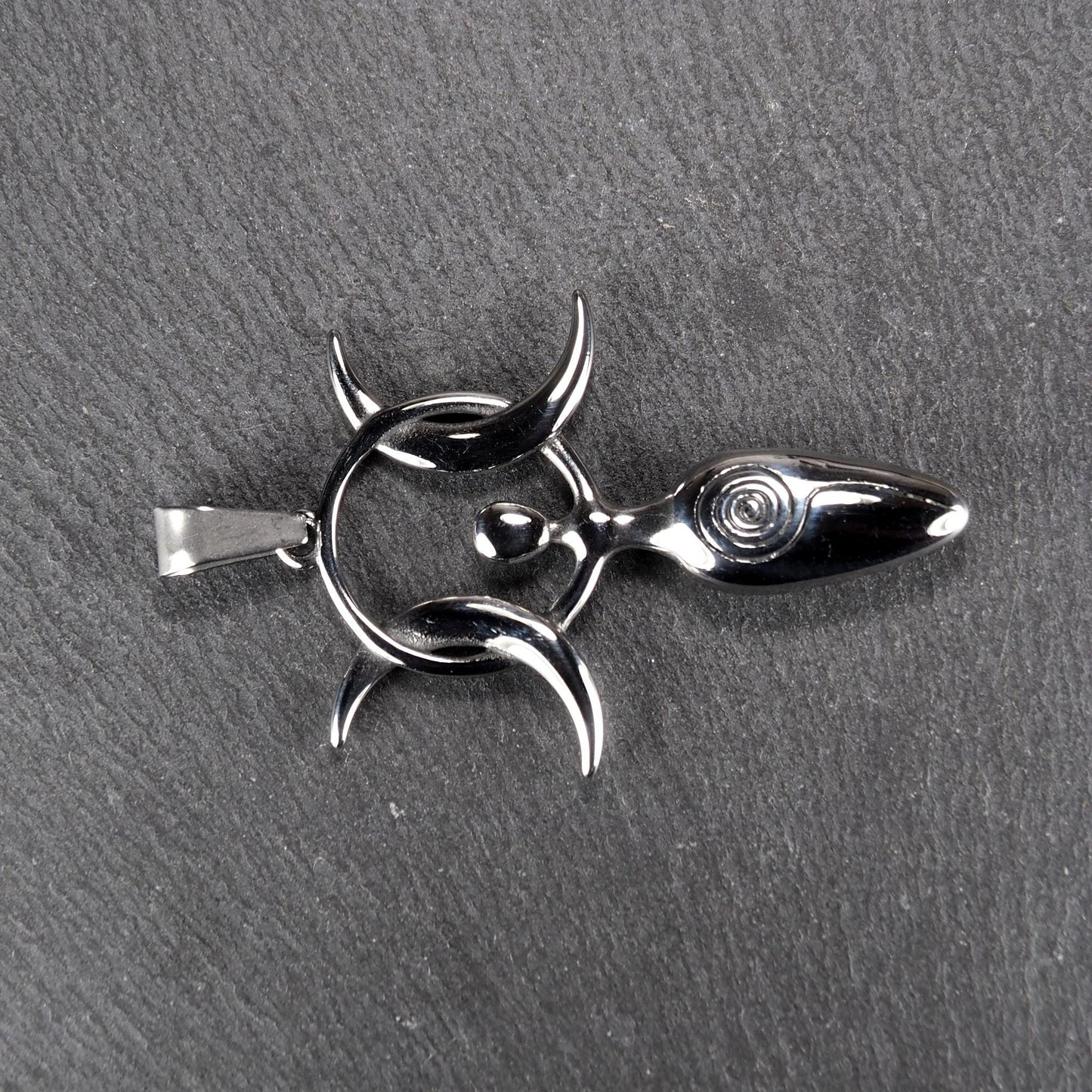 Anhänger aus poliertem silberfarbenem Edelstahl in figürlicher Form mit durchbrochenem Dreifachmond-Motiv, Spirale und Anhängerschlaufe.