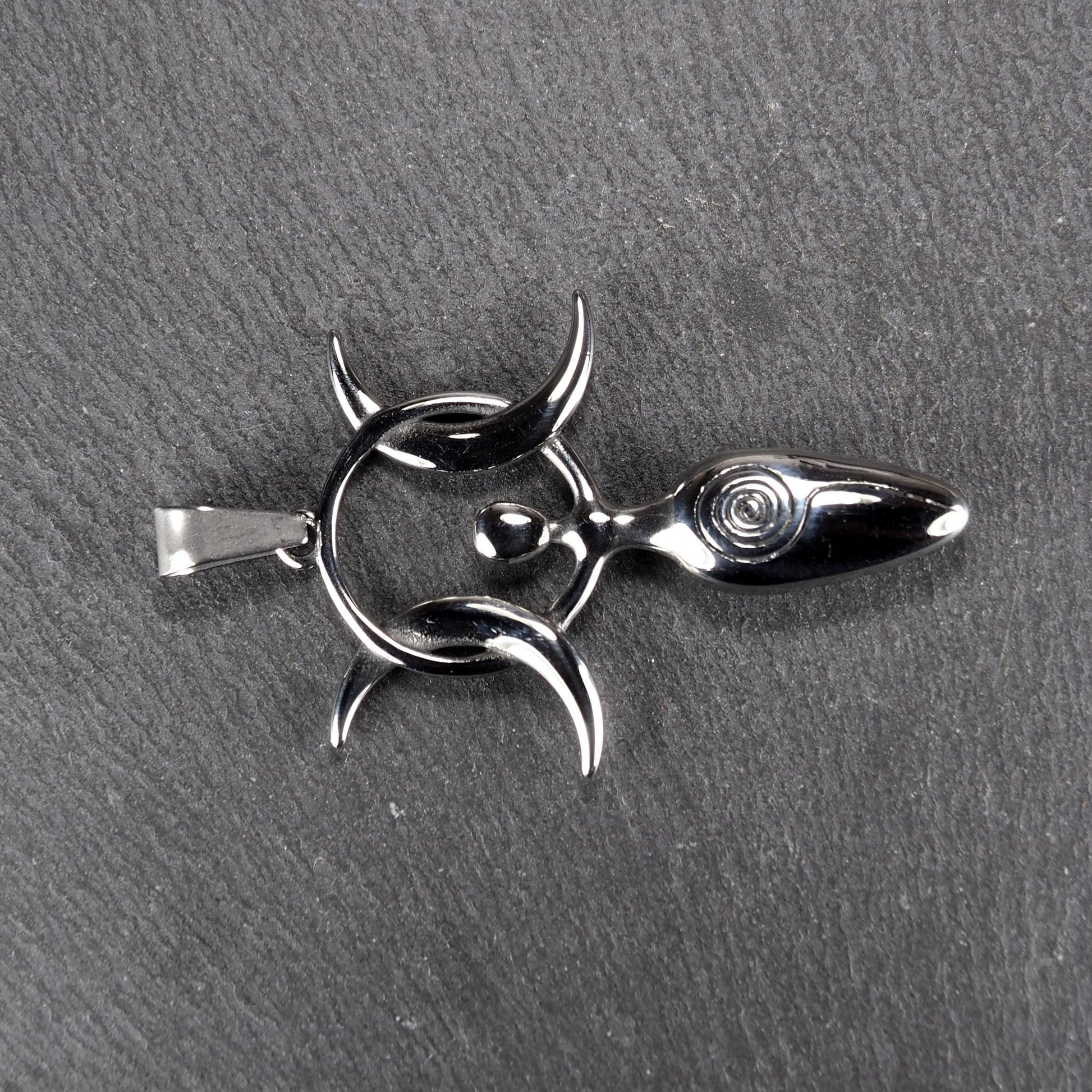 Anhänger aus poliertem silberfarbenem Edelstahl in figürlicher Form mit durchbrochenem Dreifachmond-Motiv, Spirale und Anhängerschlaufe.