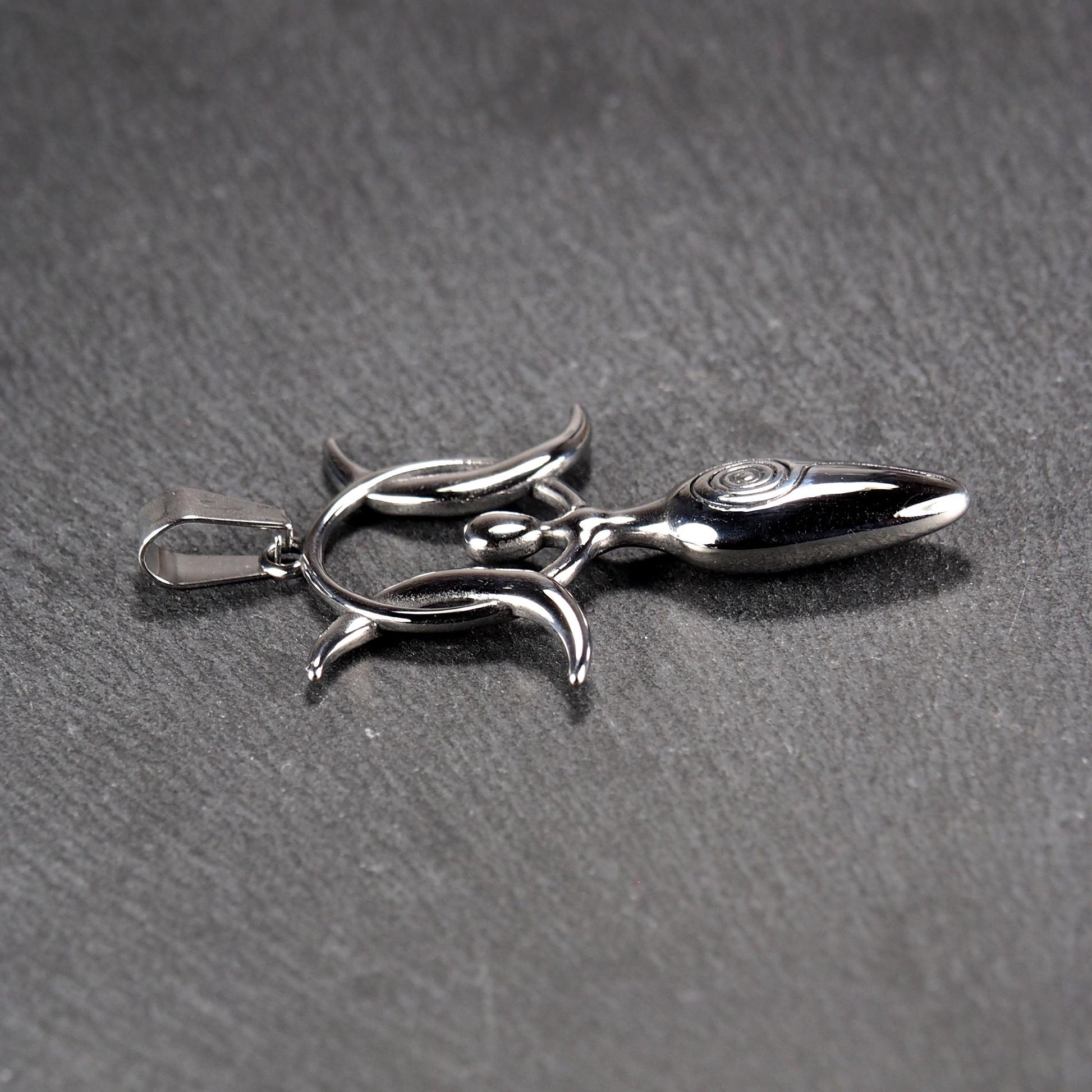 Anhänger aus poliertem silberfarbenem Edelstahl in figürlicher Form mit durchbrochenem Dreifachmond-Motiv, Spirale und Anhängerschlaufe.