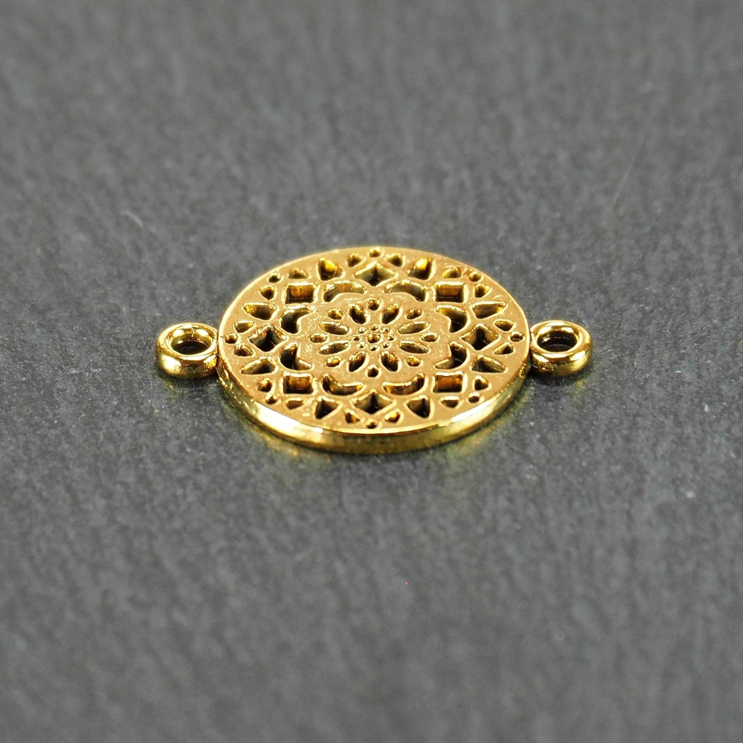 Runder goldfarbener Verbinder mit durchbrochenem, radial-symmetrischem Mandala-/Blütenmuster und zwei gegenüberliegenden Ösen.