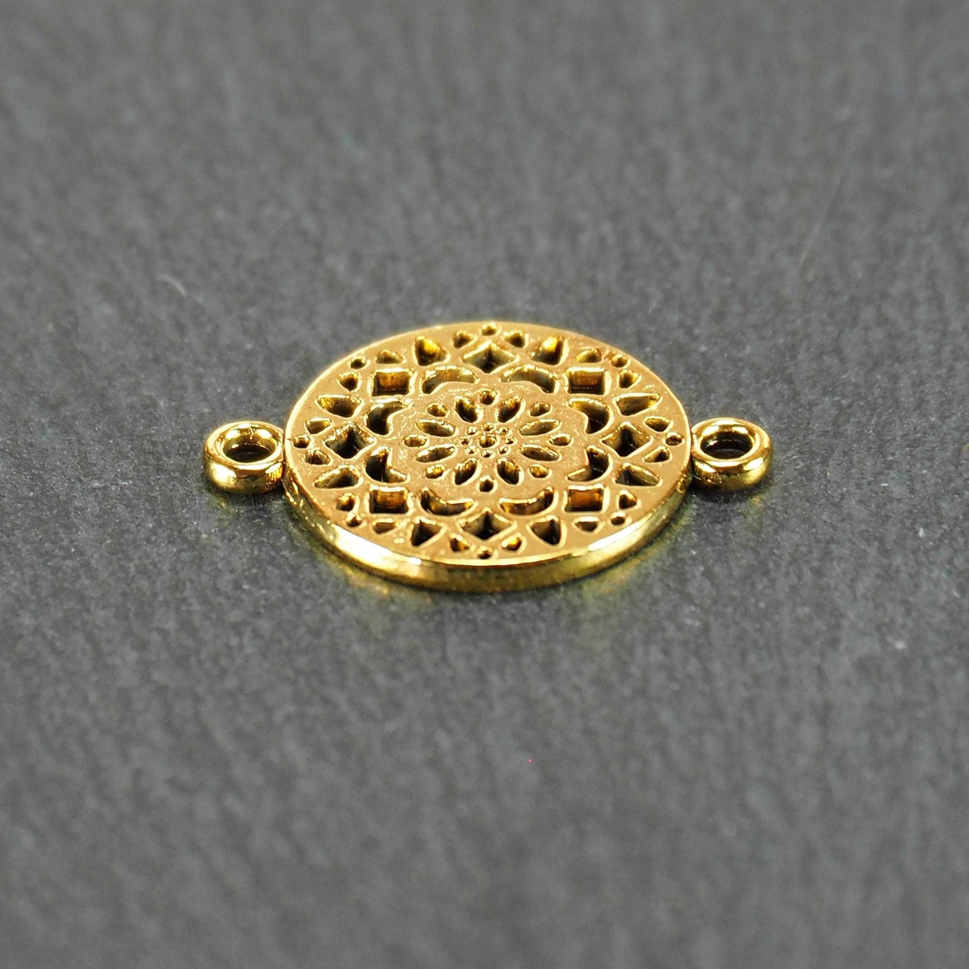 Runder goldfarbener Verbinder mit durchbrochenem, radial-symmetrischem Mandala-/Blütenmuster und zwei gegenüberliegenden Ösen.