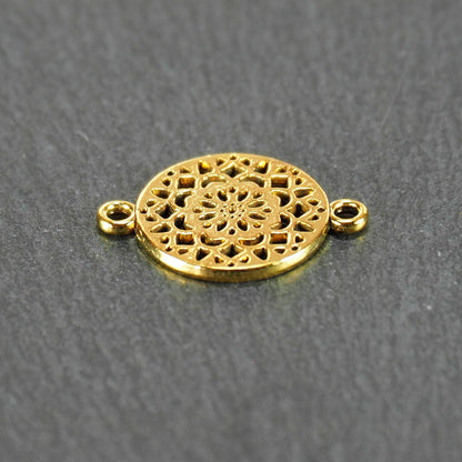 Runder goldfarbener Verbinder mit durchbrochenem, radial-symmetrischem Mandala-/Blütenmuster und zwei gegenüberliegenden Ösen.