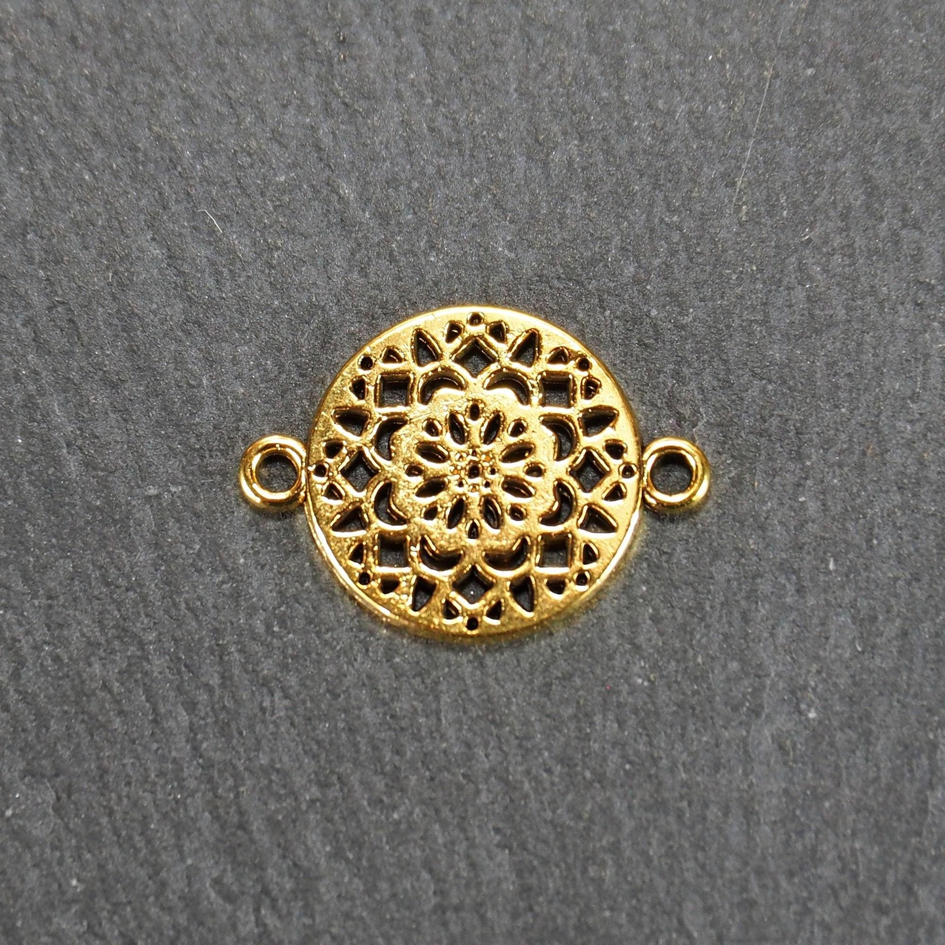 Runder goldfarbener Verbinder mit durchbrochenem, radial-symmetrischem Mandala-/Blütenmuster und zwei gegenüberliegenden Ösen.