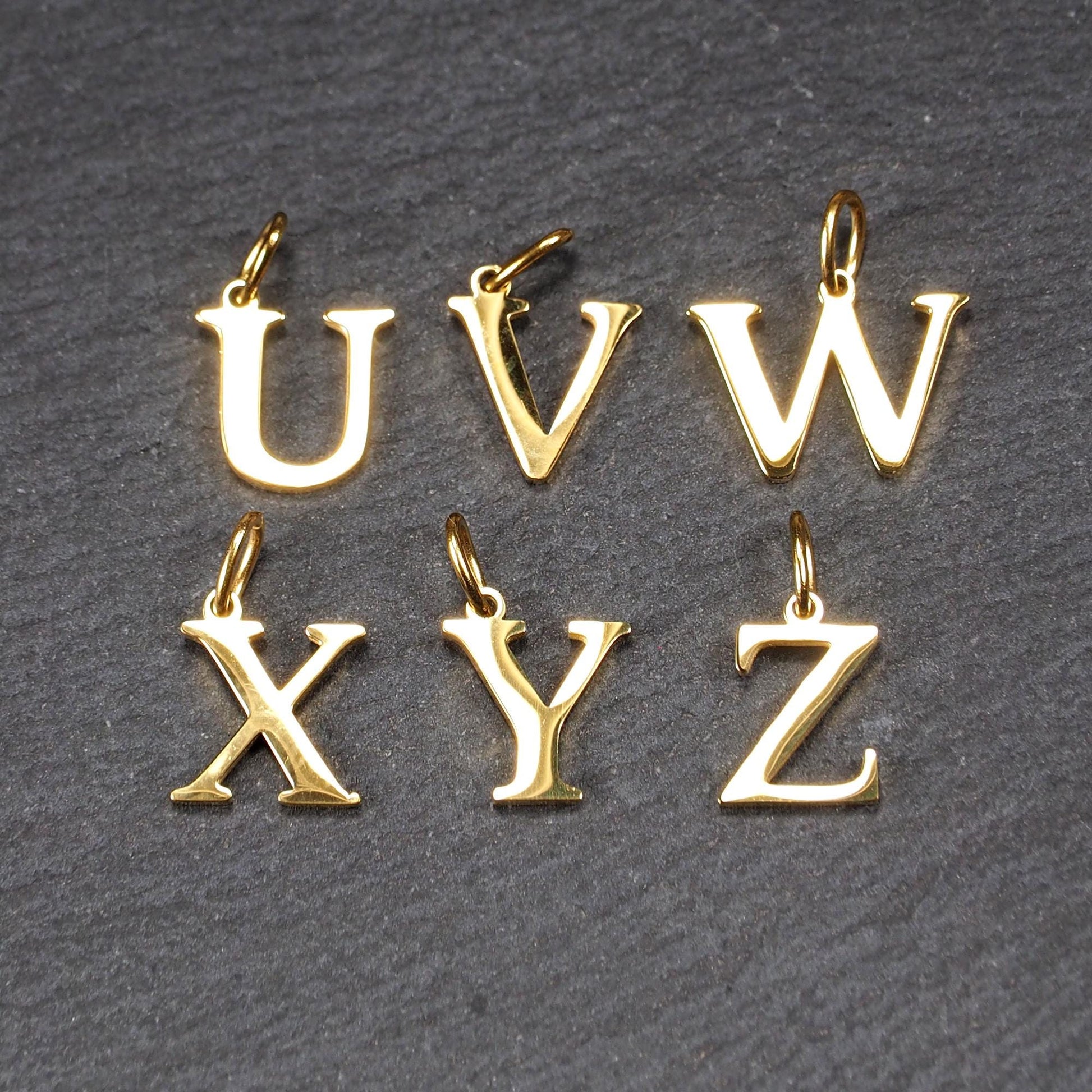 Sechs Buchstabenanhänger (U, V, W, X, Y, Z) aus vergoldetem Metall haben Versal-Serifen, glänzende Oberfläche und kleine Ösen.
