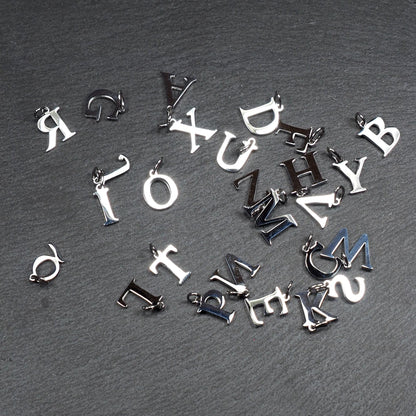 Buchstaben-Anhänger, silberne polierte Metalloberfläche, Großbuchstaben in Serifenschrift, kompakte typografische Form, jeweils mit kleiner Öse.