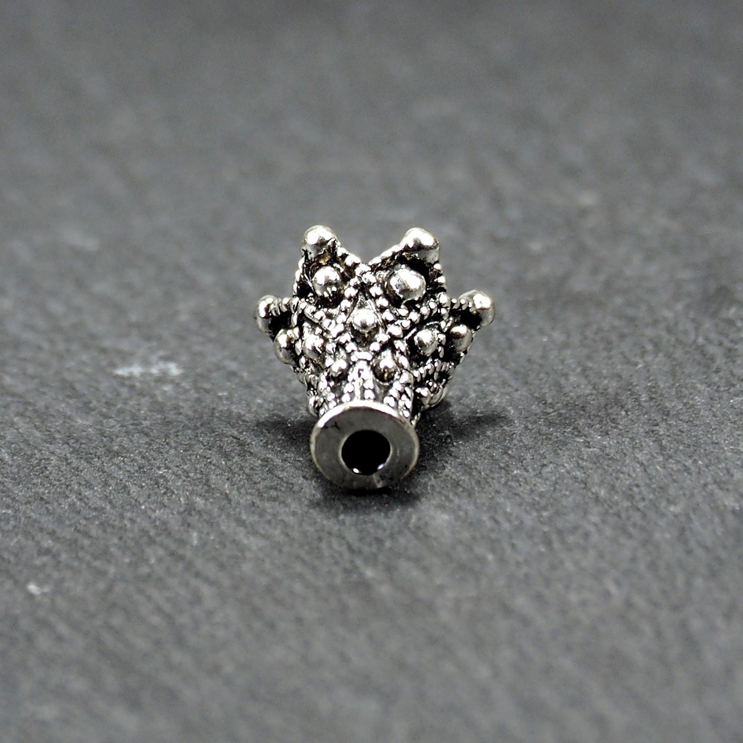 Konische, antik-silberne Perlenkappe mit durchbrochenem filigranem Ornament, reliefartigen Kugeln und sichtbarem Fädelloch oben.