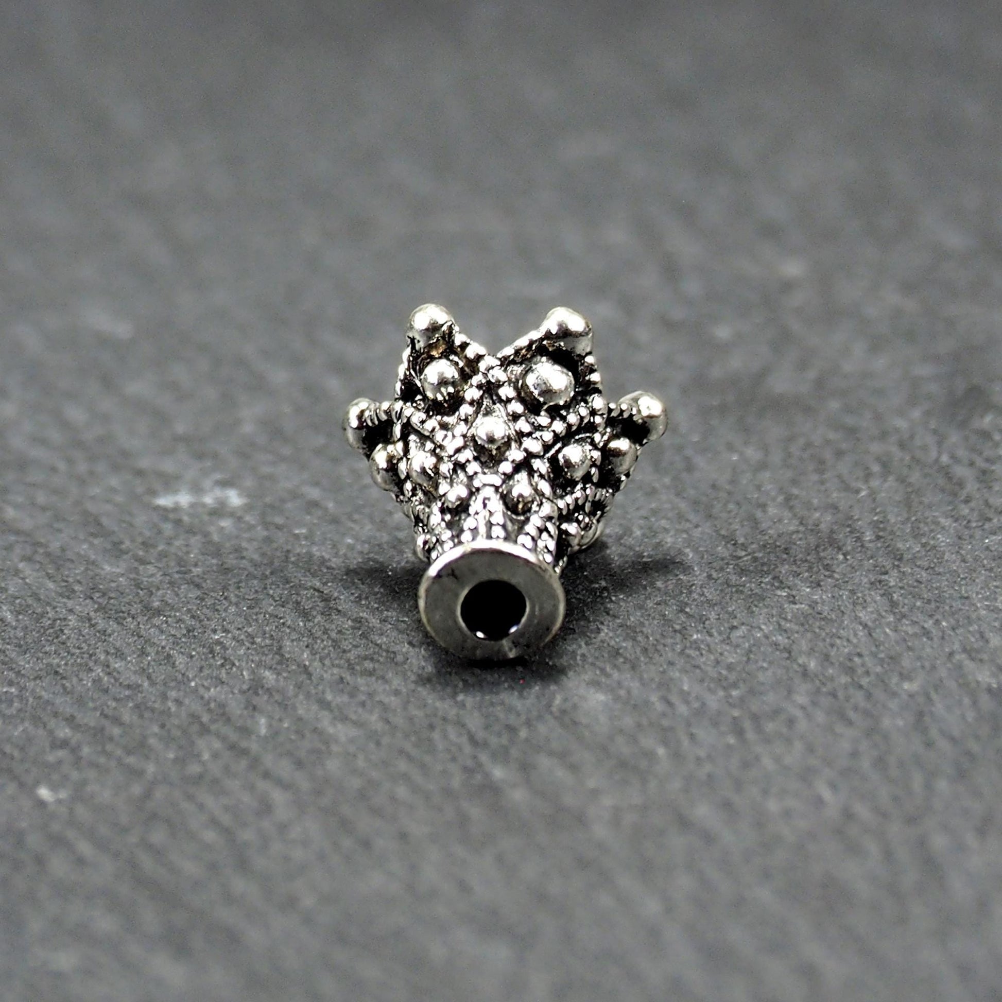 Konische, antik-silberne Perlenkappe mit durchbrochenem filigranem Ornament, reliefartigen Kugeln und sichtbarem Fädelloch oben.