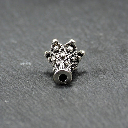 Konische, antik-silberne Perlenkappe mit durchbrochenem filigranem Ornament, reliefartigen Kugeln und sichtbarem Fädelloch oben.