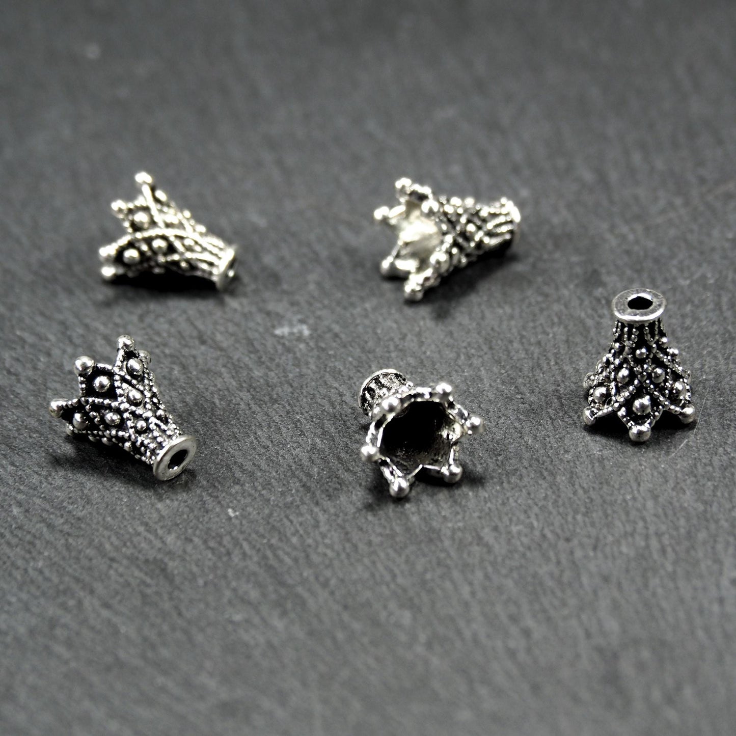 Konische, antik-silberne Perlenkappe mit durchbrochenem filigranem Ornament, reliefartigen Kugeln und sichtbarem Fädelloch oben.