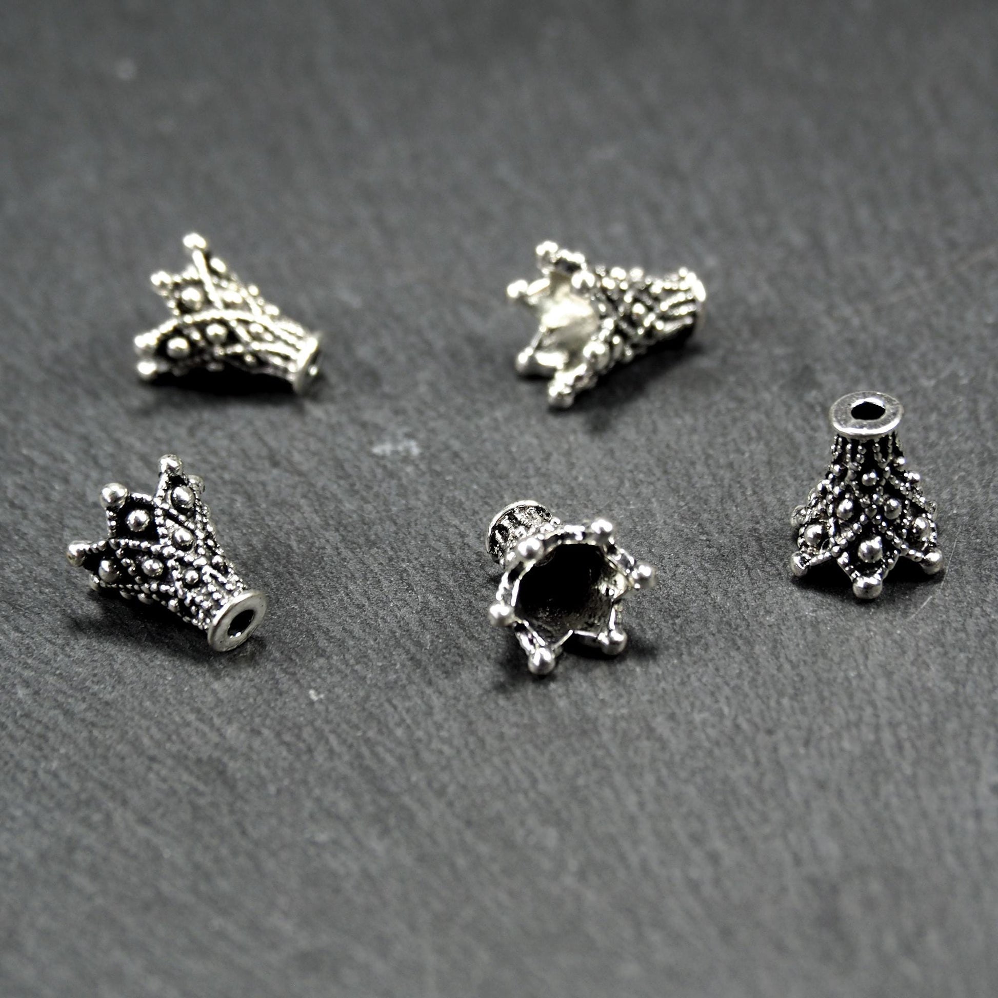 Konische, antik-silberne Perlenkappe mit durchbrochenem filigranem Ornament, reliefartigen Kugeln und sichtbarem Fädelloch oben.