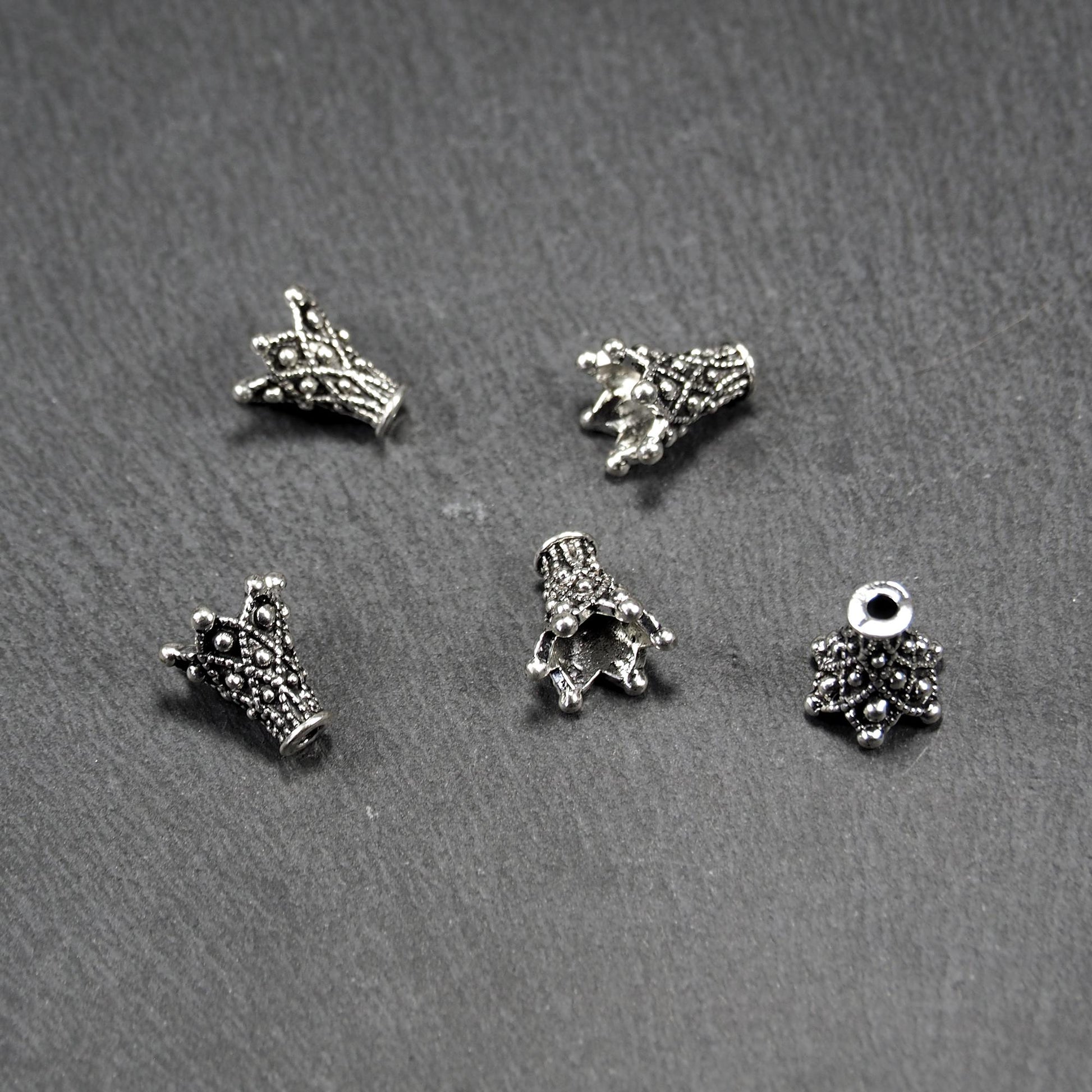 Konische, antik-silberne Perlenkappe mit durchbrochenem filigranem Ornament, reliefartigen Kugeln und sichtbarem Fädelloch oben.