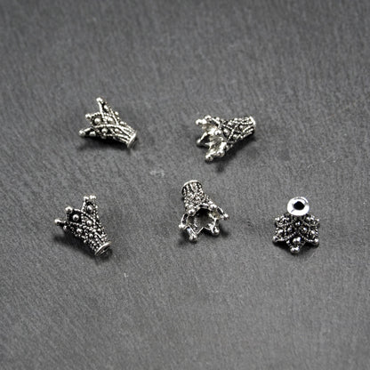 Konische, antik-silberne Perlenkappe mit durchbrochenem filigranem Ornament, reliefartigen Kugeln und sichtbarem Fädelloch oben.