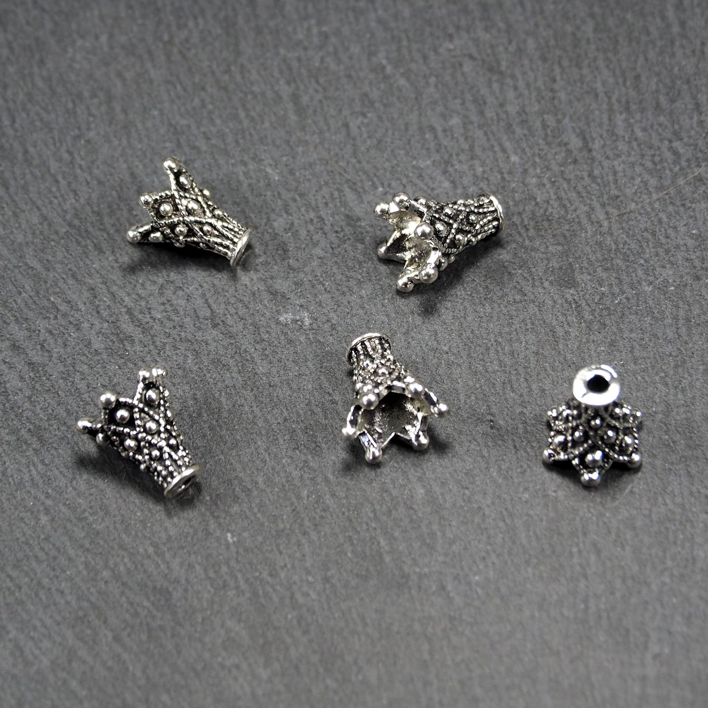 Konische, antik-silberne Perlenkappe mit durchbrochenem filigranem Ornament, reliefartigen Kugeln und sichtbarem Fädelloch oben.