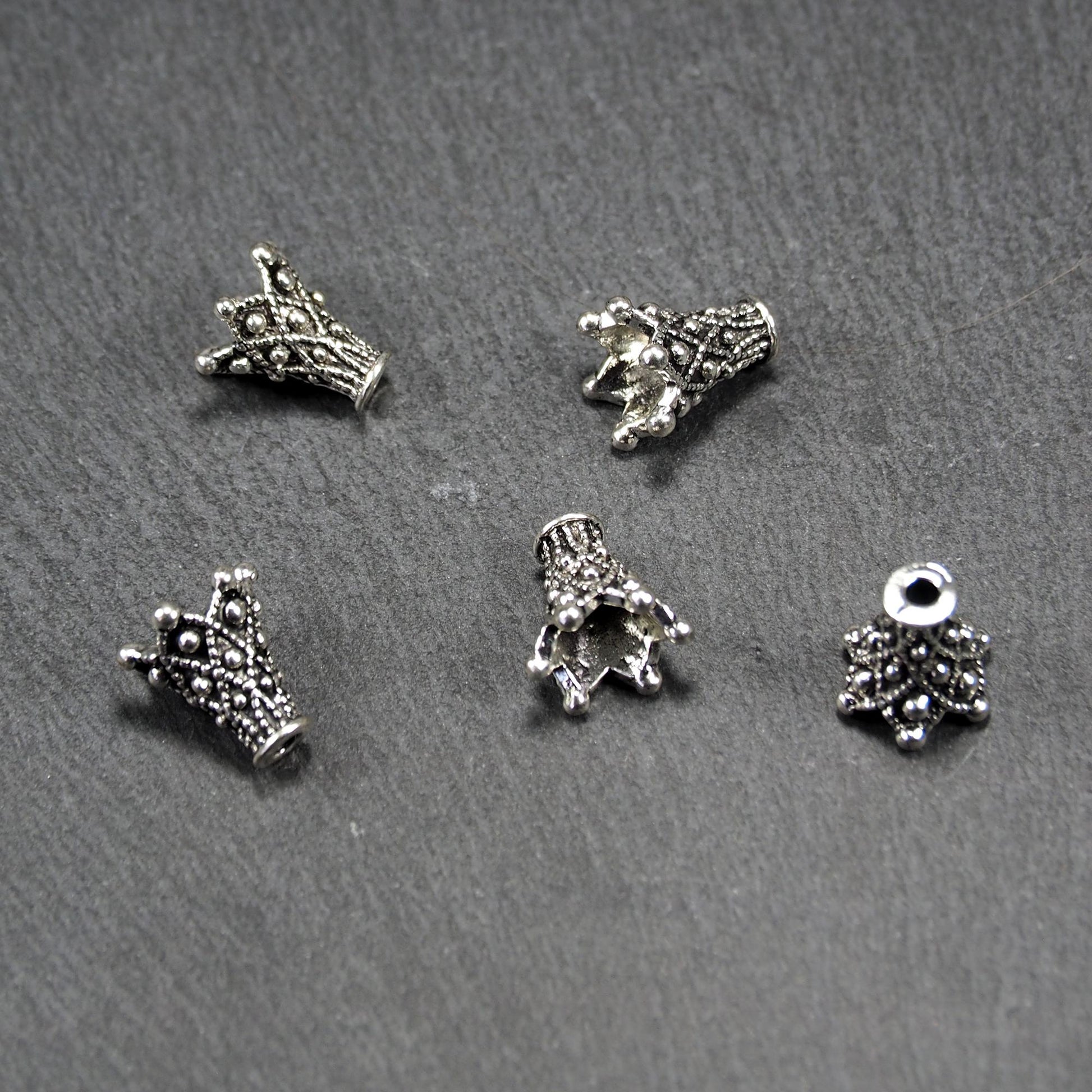 Konische, antik-silberne Perlenkappe mit durchbrochenem filigranem Ornament, reliefartigen Kugeln und sichtbarem Fädelloch oben.