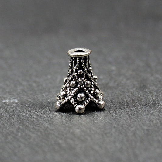 Konische, antik-silberne Perlenkappe mit durchbrochenem filigranem Ornament, reliefartigen Kugeln und sichtbarem Fädelloch oben.