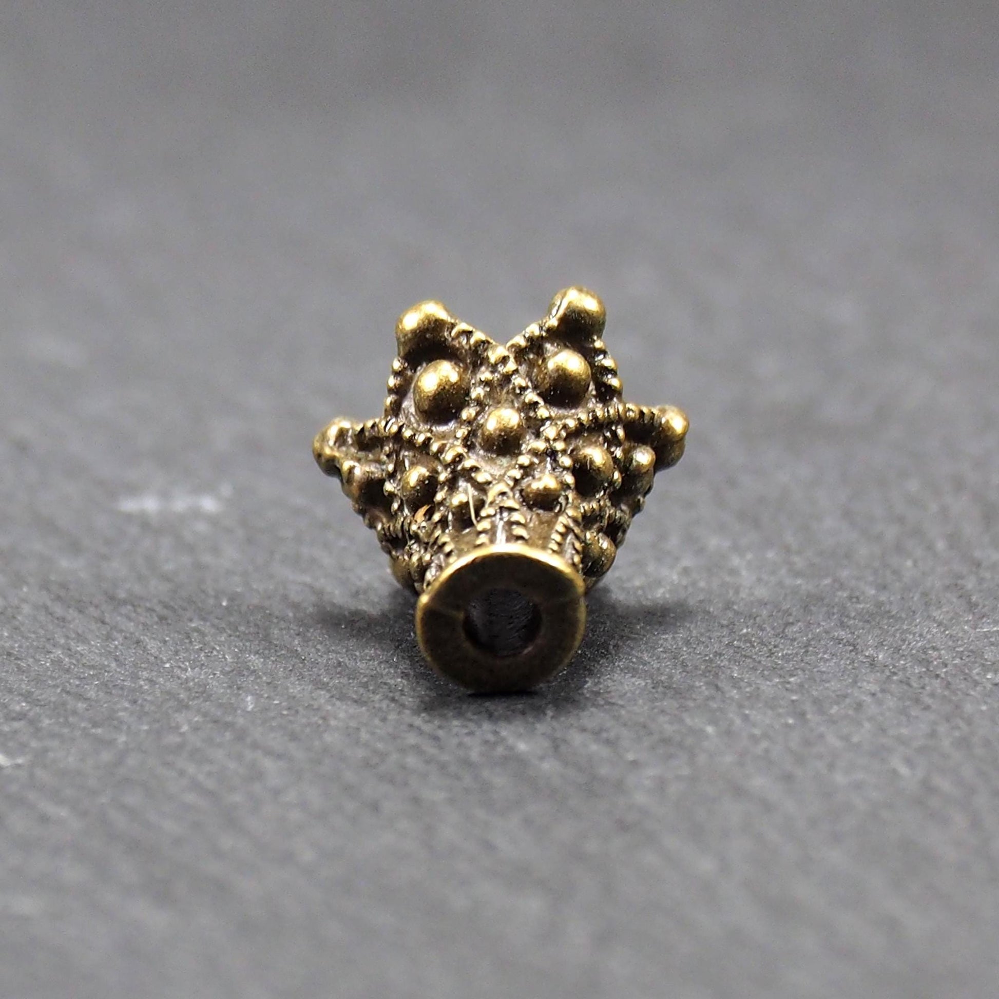 Konische bronzefarbene Perlenkappe aus Metall mit filigranem Ornamentreliéf, kugeligen Verzierungen und zentralem Fädelloch.