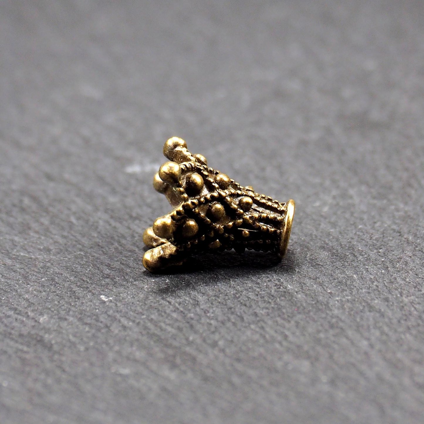 Konische bronzefarbene Perlenkappe aus Metall mit filigranem Ornamentreliéf, kugeligen Verzierungen und zentralem Fädelloch.