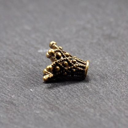 Konische bronzefarbene Perlenkappe aus Metall mit filigranem Ornamentreliéf, kugeligen Verzierungen und zentralem Fädelloch.