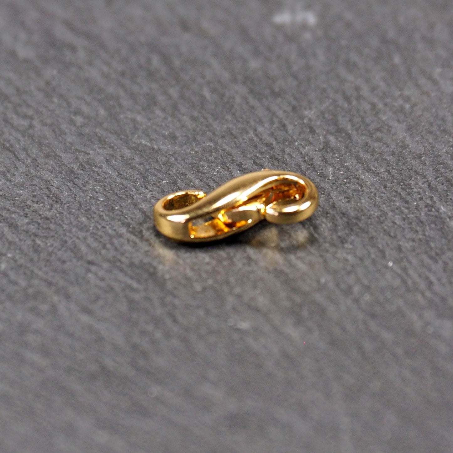 Karabiner in liegender Acht, goldfarbenes glänzendes Metall mit glatter Oberfläche, zwei gegenüberliegende Öffnungen und sichtbaren Ringösen.