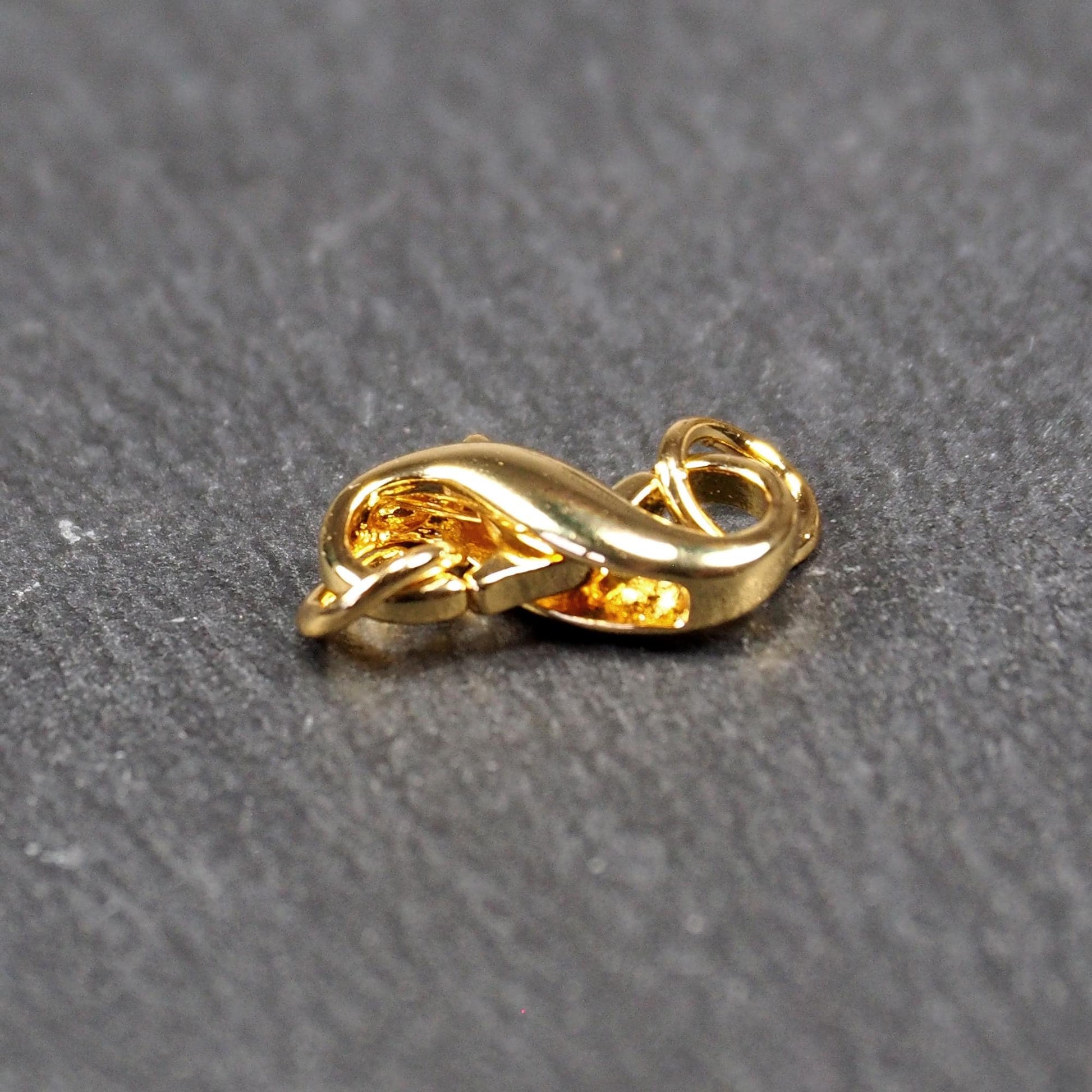 Karabiner in liegender Acht, goldfarbenes glänzendes Metall mit glatter Oberfläche, zwei gegenüberliegende Öffnungen und sichtbaren Ringösen.