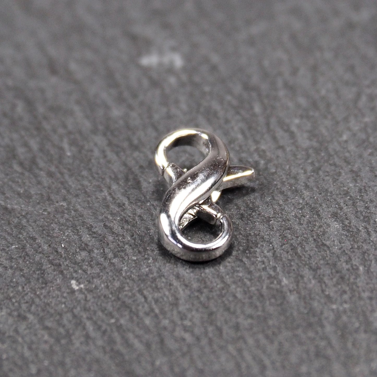 Ein doppelseitiger Karabiner im liegenden Acht-Design, silberfarben glänzend mit organisch geschwungener, durchbrochener Form und integrierter Öse.