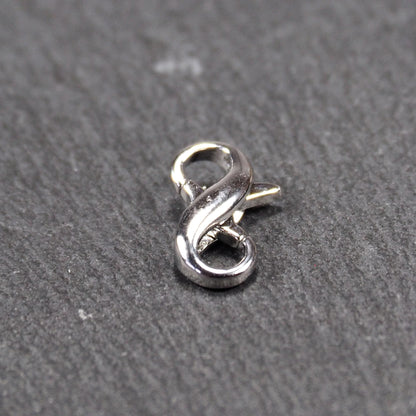 Ein doppelseitiger Karabiner im liegenden Acht-Design, silberfarben glänzend mit organisch geschwungener, durchbrochener Form und integrierter Öse.