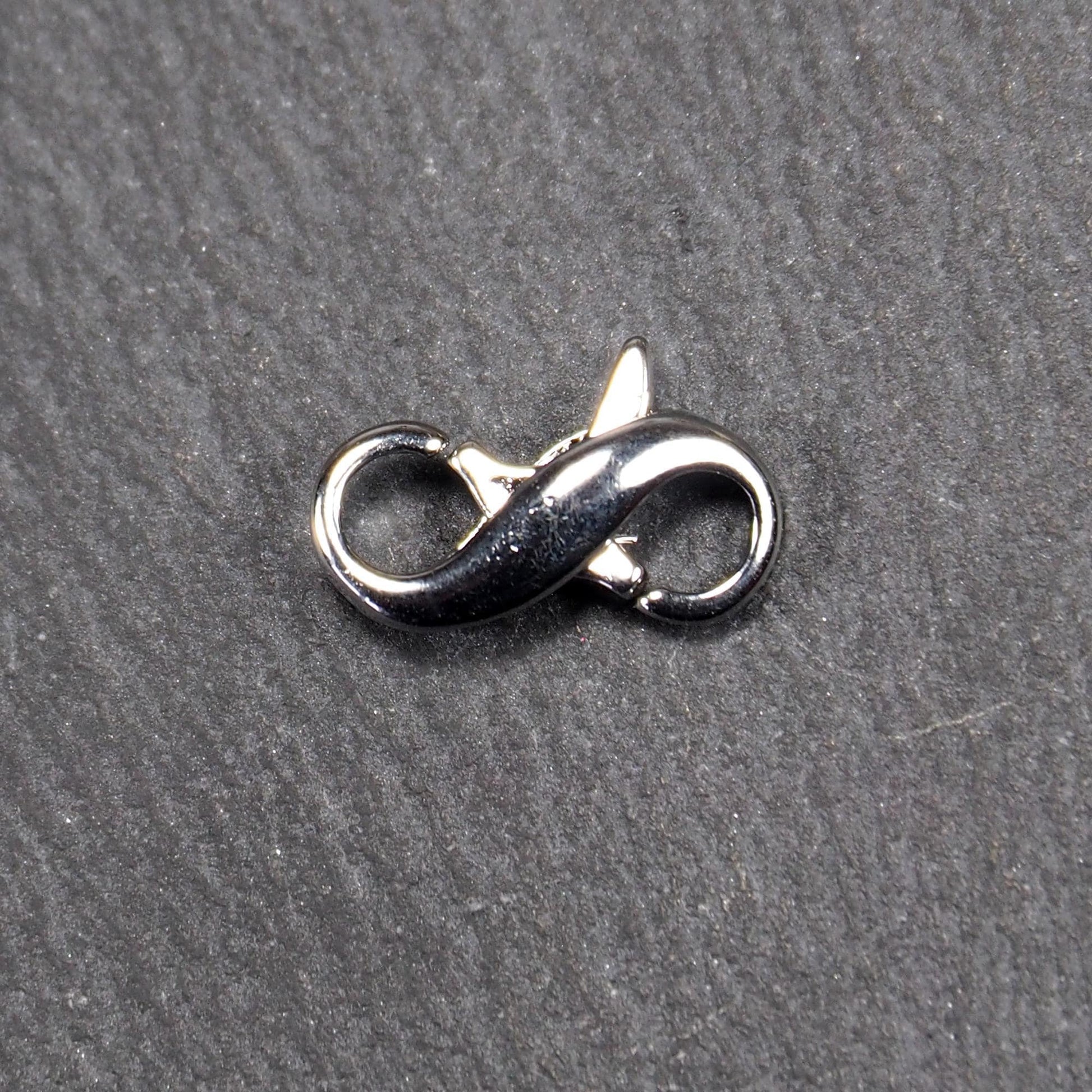 Ein doppelseitiger Karabiner im liegenden Acht-Design, silberfarben glänzend mit organisch geschwungener, durchbrochener Form und integrierter Öse.